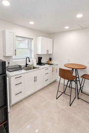 A modern kitchen with white cabinets, a marble countertop, a coffee maker, and a round wooden table with two chairs. - New Listing (Bradenton)