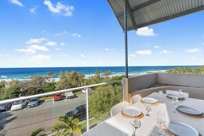 En balkon med et spisebord, der giver udsigt over en parkeringsplads og havet.