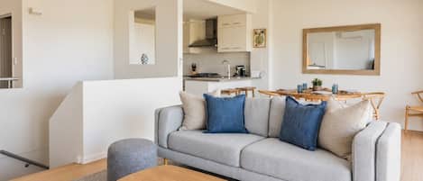 A modern living room with a grey sofa, wooden coffee table, and a kitchen in the background.