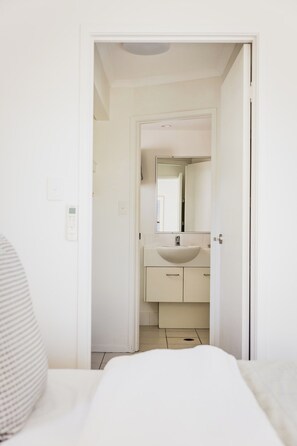 Ein Hotelzimmer mit einem Bett, einem Nachttisch, einem Badezimmer mit Waschbecken und Spiegel sowie einer Tür zu einem weiteren Raum.