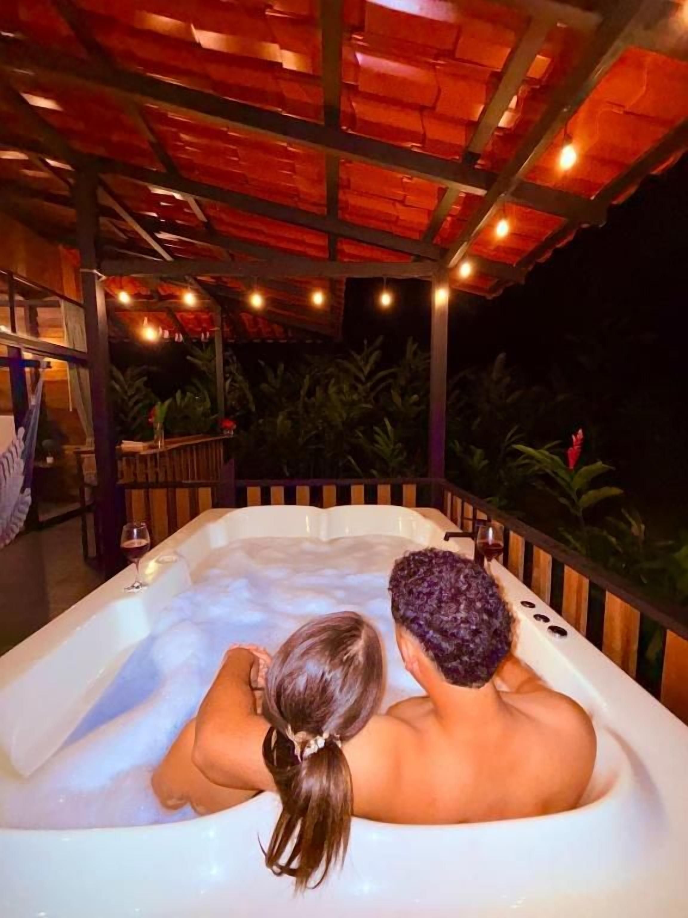 A couple in a hot tub under a wooden pergola at night.