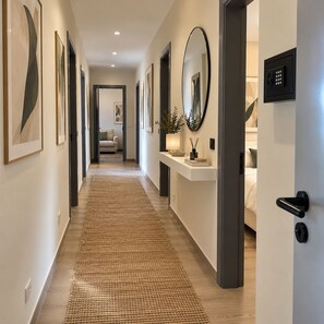 Un pasillo con obras de arte enmarcadas, un espejo, una puerta con cerradura electrónica y una cama al fondo.