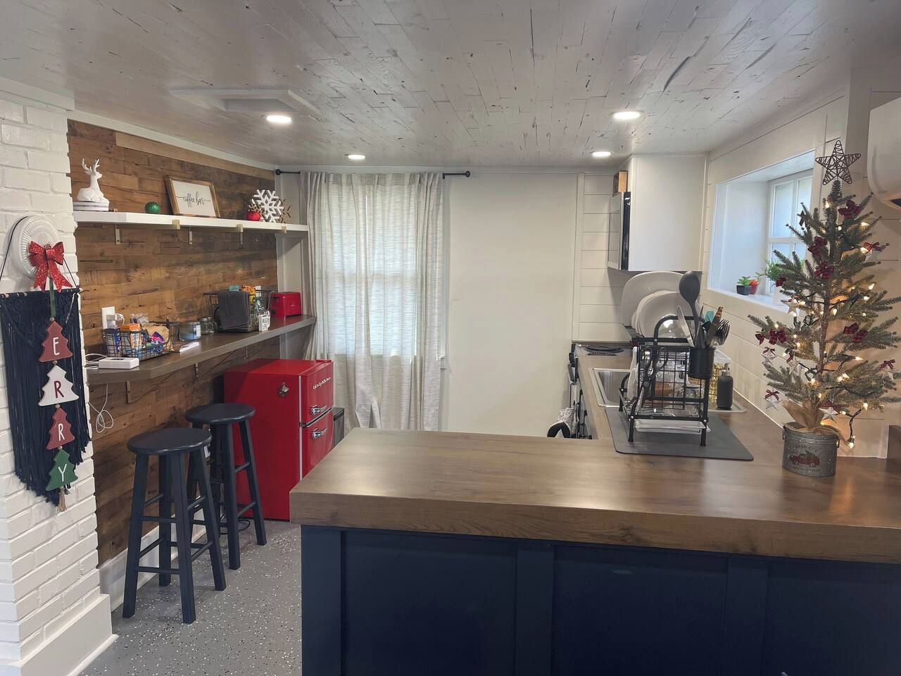 Een keuken met een houten aanrecht, barstoelen, een rode koelkast en een kerstboom.