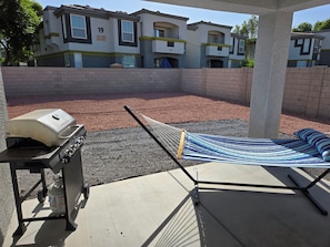 Ein Garten mit Grill, Hängematte und einer gepflasterten Terrasse.