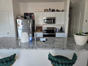 Eine Küche mit Kühlschrank, Mikrowelle, Backofen und Arbeitsplatten aus Granit.