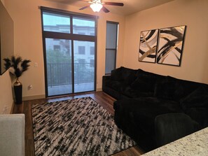 Ein Wohnzimmer mit einem dunkelgrauen Sofa, einem gemusterten Teppich, einer Vase mit Dekoration aus Federn und zwei abstrakten Bildern an der Wand.