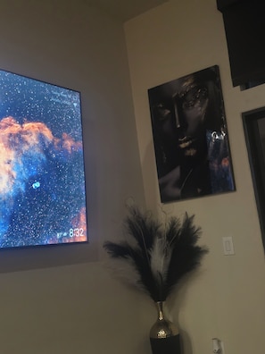 Ein Zimmer mit einem großen Bildschirm, der einen Sternenhimmel zeigt, einem gerahmten Kunstwerk darüber und einer dekorativen Vase mit Federn.