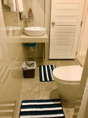 Ein Badezimmer mit Waschbecken, Toilette und Handtuchhalter. Auf dem Boden liegen zwei Streifen Teppiche.