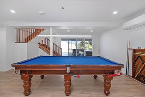 A pool table with a wooden frame and blue felt, a staircase with wooden railings, and a view through a glass door. - Zilzie Beach House! (Zilzie)