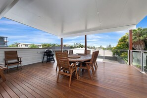 A covered outdoor patio with a wooden table and chairs, a grill, and a view of the neighborhood. - Zilzie Beach House! (Zilzie)