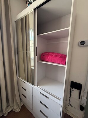 Ein Zimmer mit einem weißen Kleiderschrank, einem Spiegel und einem pinken Handtuch auf der obersten Ablage.