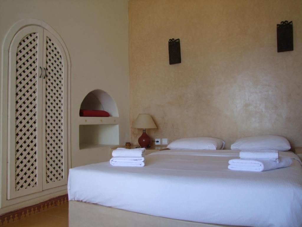 Una habitación de hotel con una cama, una mesita de noche, una lámpara y un armario con diseño de celosía.