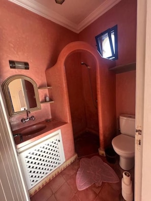 Une salle de bain avec un mur rose, un lavabo blanc, un miroir, une douche et des toilettes.