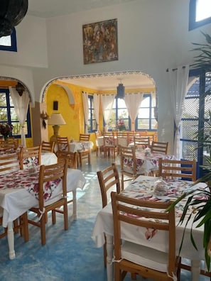 Un comedor con varias mesas y sillas, una araña y un cuadro en la pared.