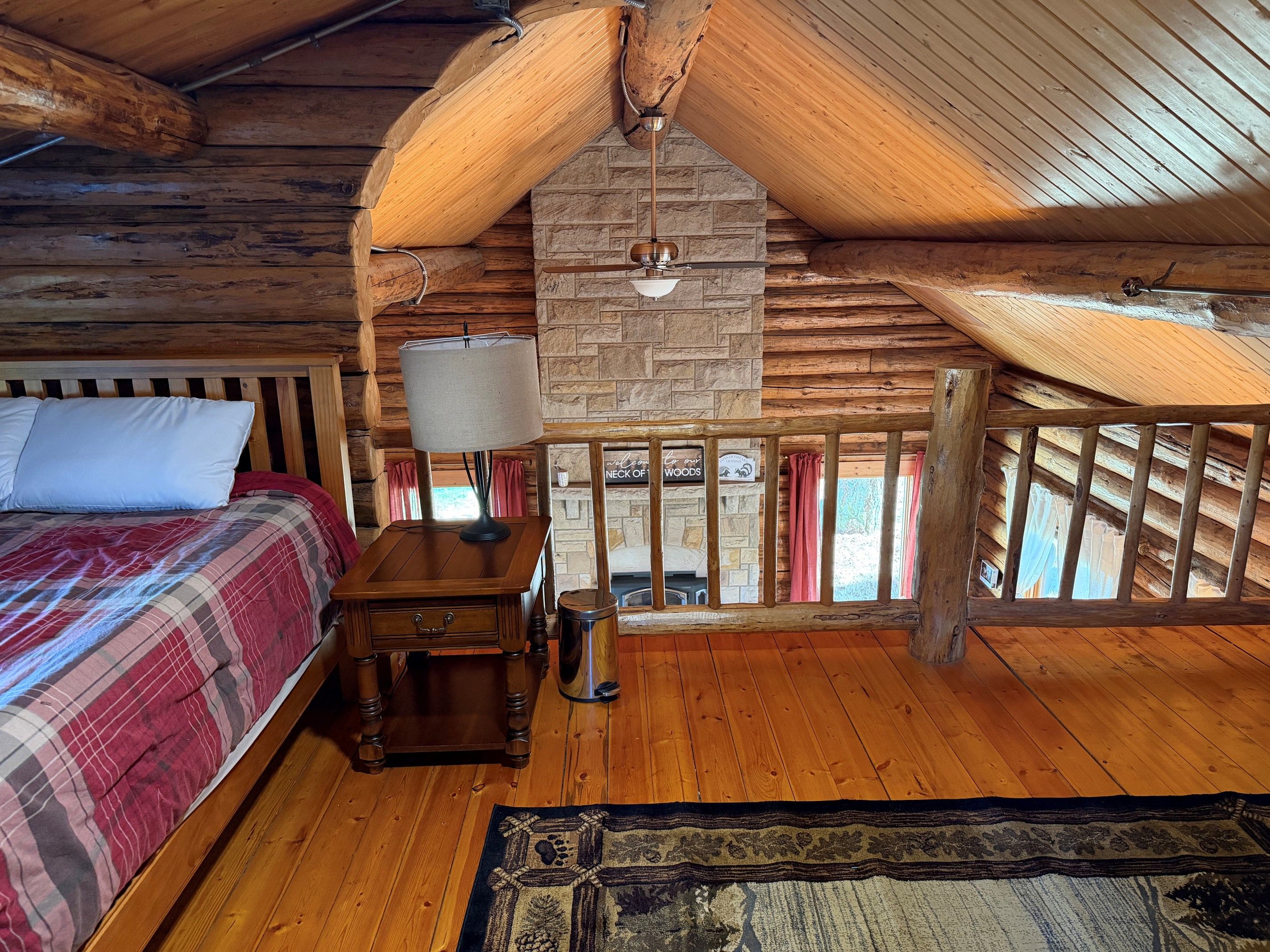 Een knus houten slaapkamer met een bed, nachtkastje, lamp en uitzicht op de natuur.