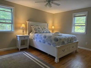 A bedroom with a bed, nightstands, a ceiling fan, and two windows.