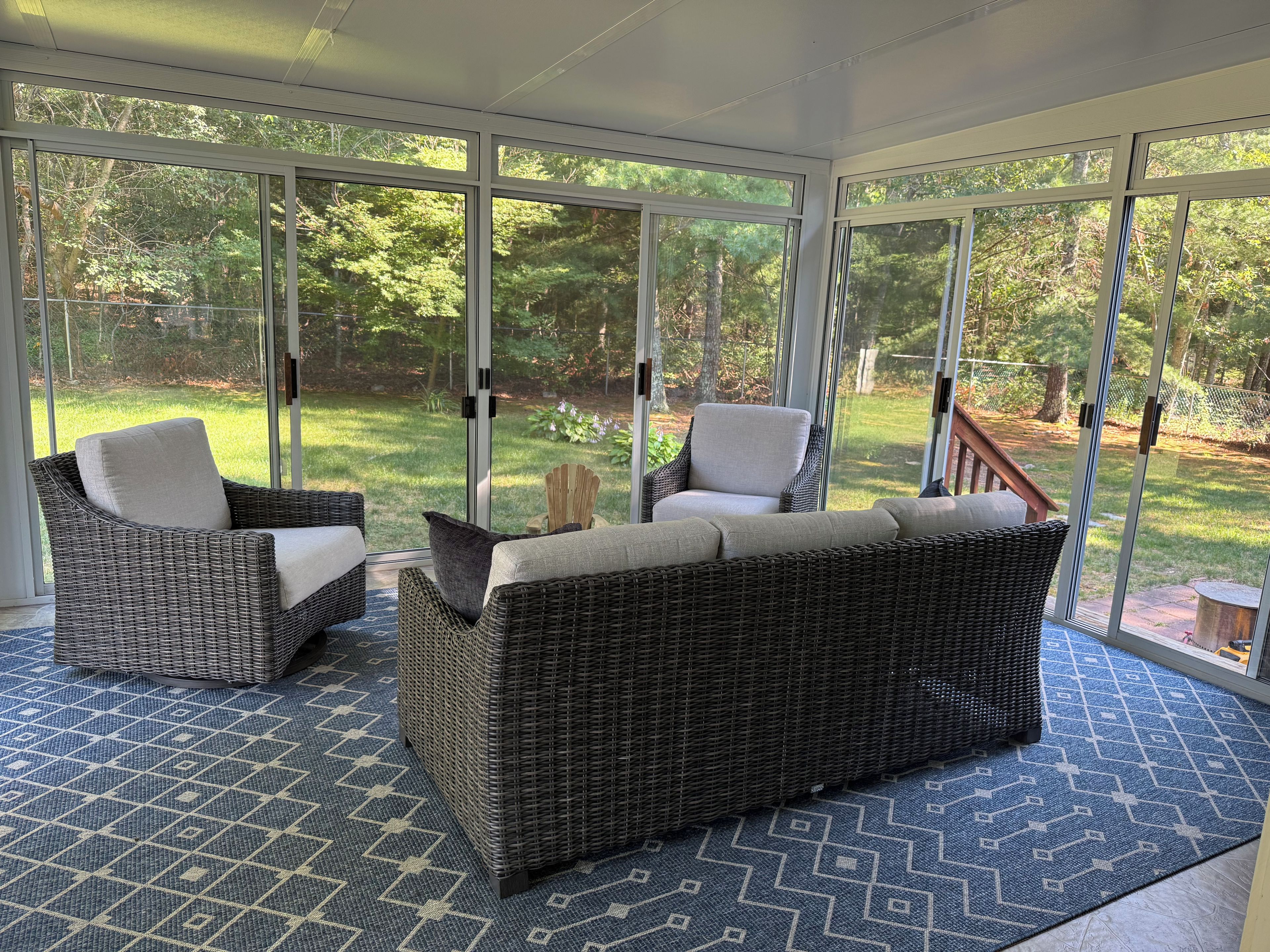 A sunroom with wicker furniture, large windows, and a patterned floor.