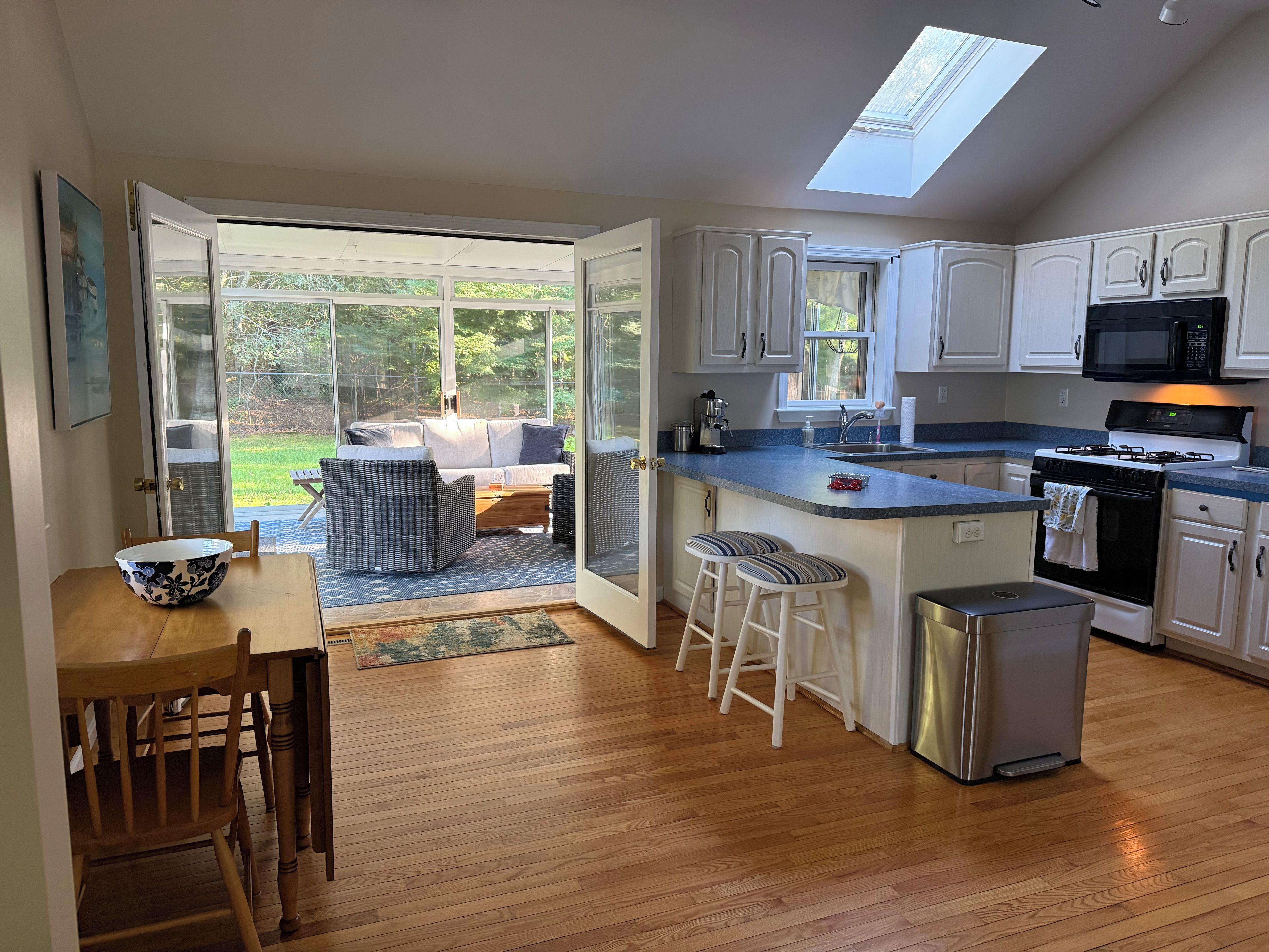 A modern kitchen with white cabinets, a stainless steel refrigerator, and a skylight.
