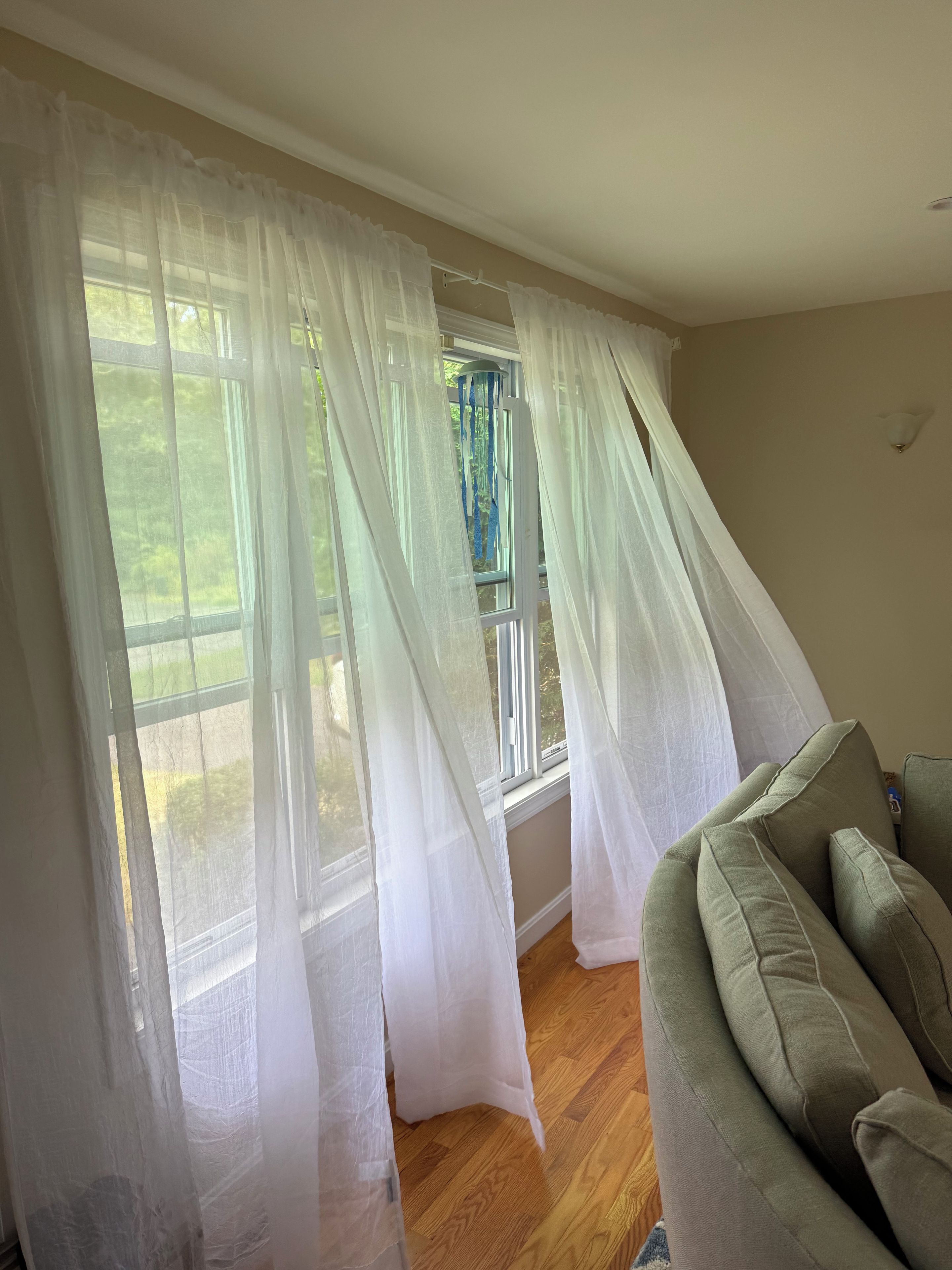 Una habitación con un ventanal grande cubierto por cortinas translúcidas, un sofá verde y piso de madera.
