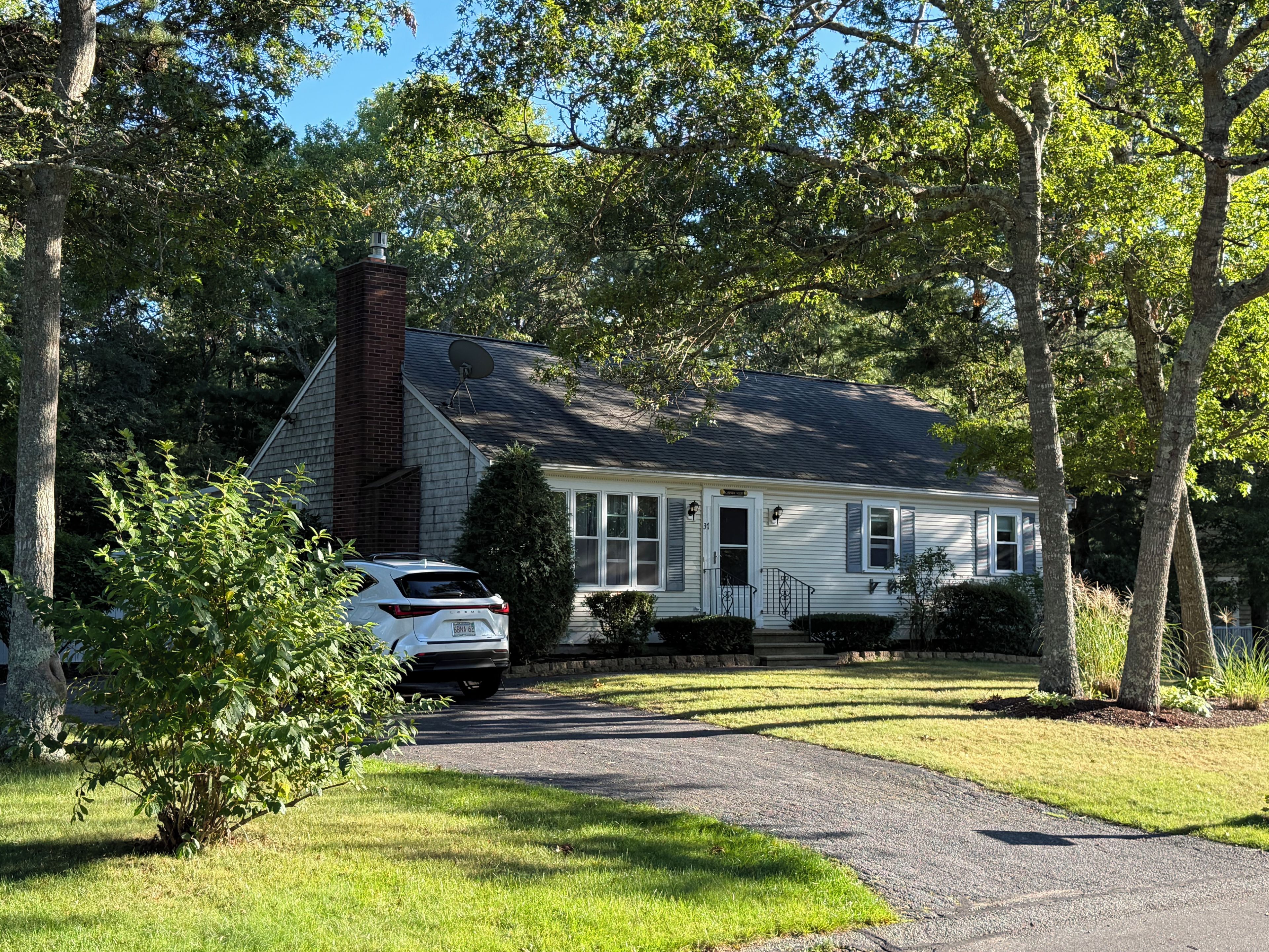 A two-story house with a brick chimney, a satellite dish, and a driveway leading to a parked car.