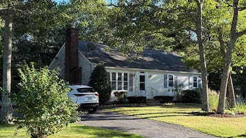 A two-story house with a brick chimney, a satellite dish, and a driveway leading to a parked car.