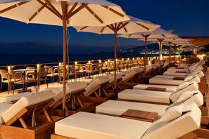 Une rangée de chaises longues avec des parasols, une terrasse en bois et une vue sur la mer au crépuscule.