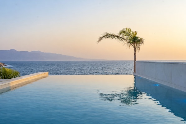 Une piscine à débordement offrant une vue sur la mer et les montagnes en arrière-plan.