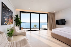Une chambre moderne dotée d’une grande porte-fenêtre coulissante donnant sur un balcon avec vue sur la mer.