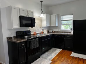 A kitchen with white cabinets, a black stove, and a window with blinds. - CatalpaCorner 2-Bed Sit & Escape/Turnkey/Mid-term/Monthly/Weekly (Springfield)