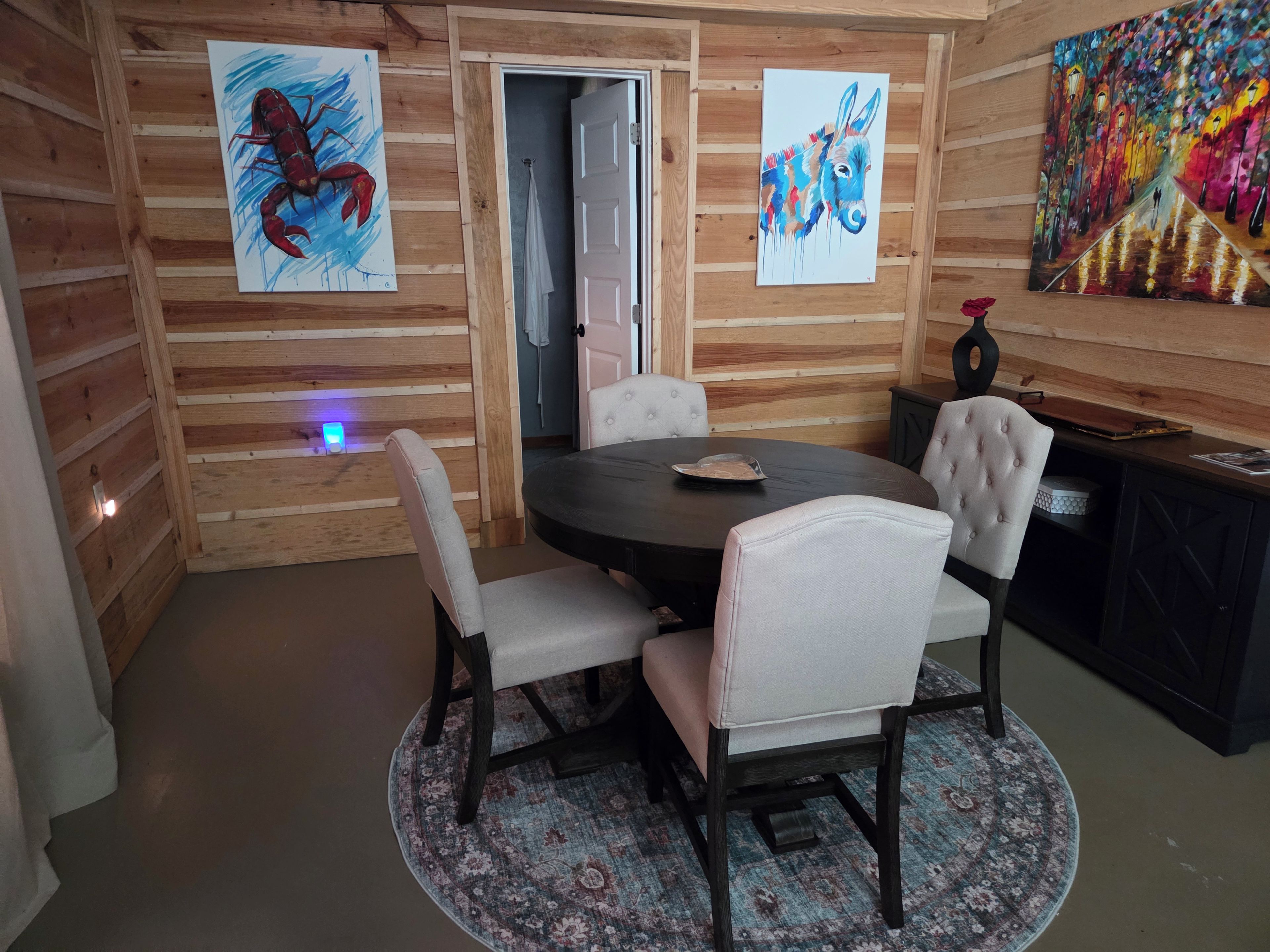 A wooden cabin interior with a round dining table, four upholstered chairs, and artwork on the walls.