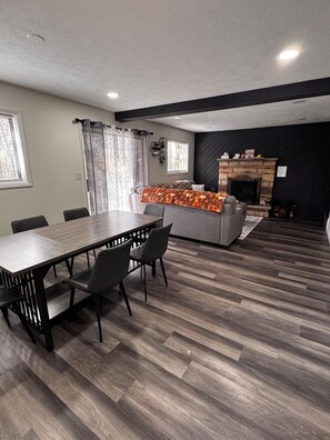 A modern living room with a dining area, fireplace, and large windows. - Cozy 3-bedroom house in enchanting Tobyhanna for your getaway (Tobyhanna)