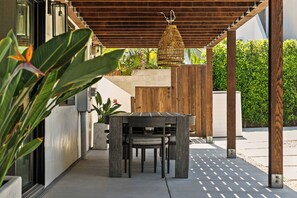 An outdoor patio area with a wooden pergola, a table with chairs, and a hanging light fixture. - Ocean View Balcony King Suite Golf Cart and AC (Oceanside)