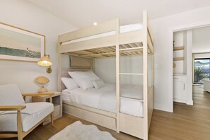 A bunk bed with a wooden frame, a bedside table with a lamp, a chair, and a rug. - Ocean View Balcony King Suite Golf Cart and AC (Oceanside)