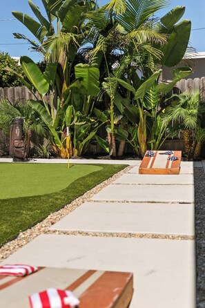 A backyard with a putting green, a golf bag, and a wooden table with American flags. - Ocean View Balcony King Suite Golf Cart and AC (Oceanside)