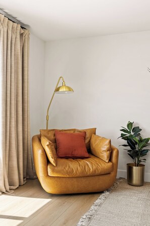 A room with a leather sofa, a floor lamp, a potted plant, and a large window with curtains. - Ocean View Balcony King Suite Golf Cart and AC (Oceanside)