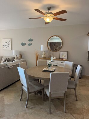 A dining area with a round table, chairs, a ceiling fan, wall decor, and a mirror. - Luxury Cabo Condo with Ocean Views Overlooking Cabo Real Golf Course (San José del Cabo)