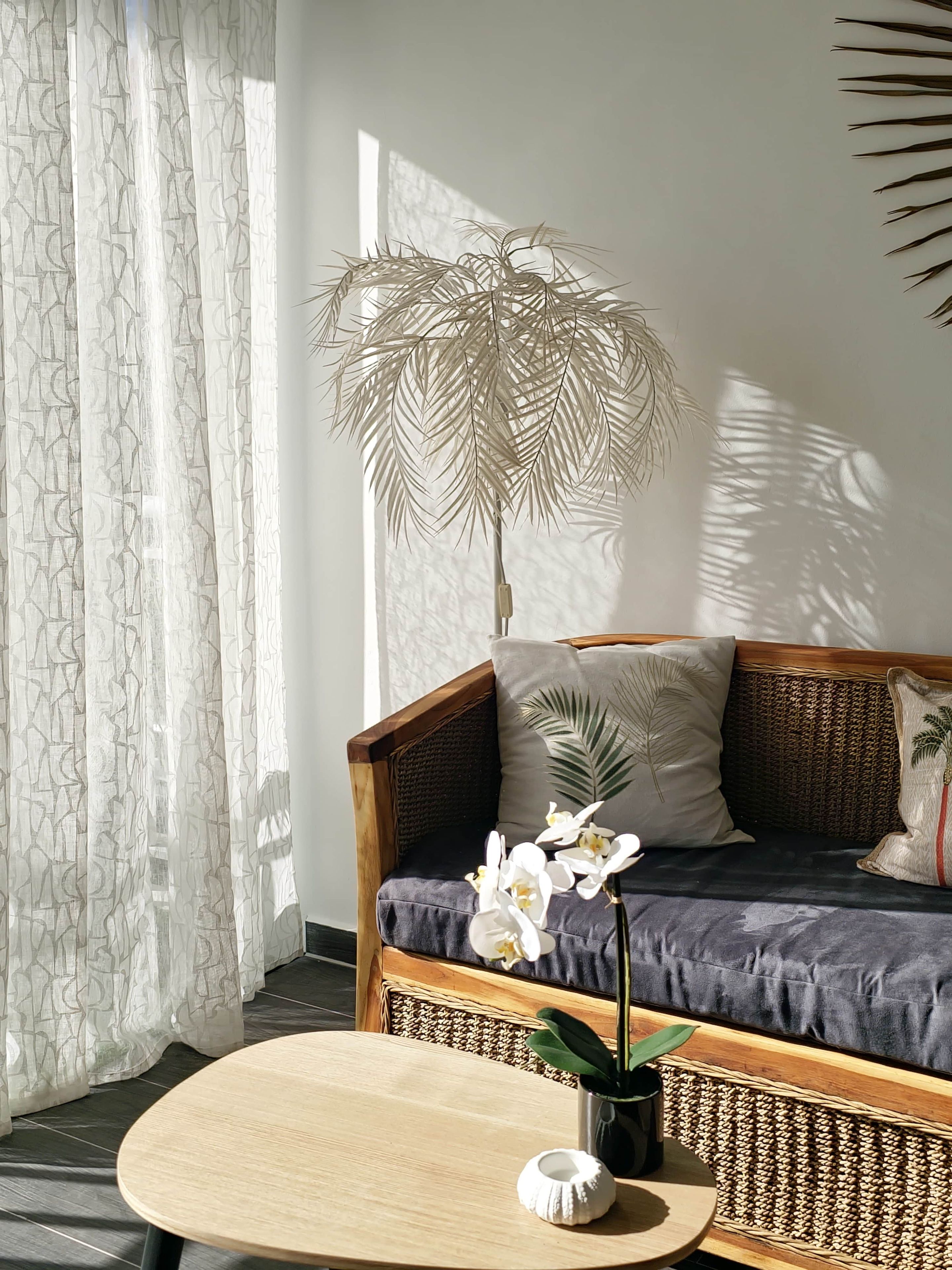 A room with a wooden sofa, a round wooden table, and a tall plant.