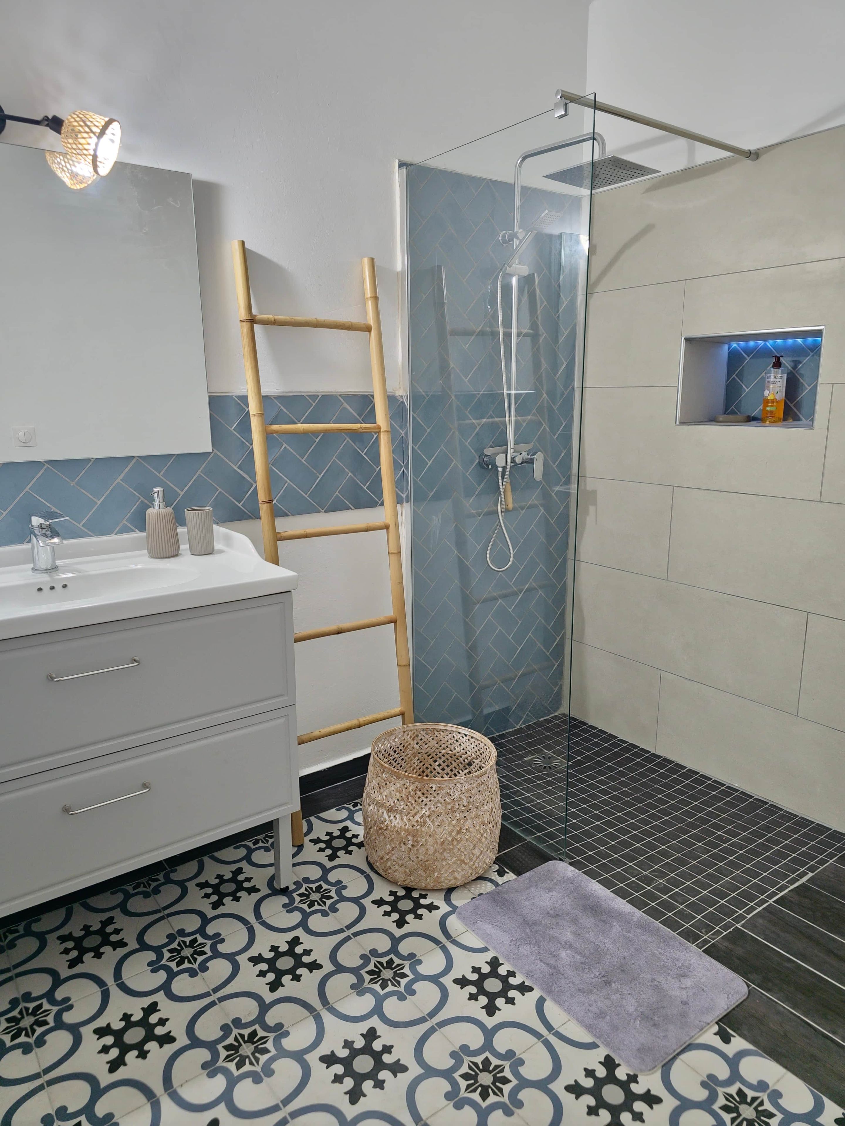 A bathroom with a shower, a vanity with a mirror, a towel, and a small shelf with toiletries.