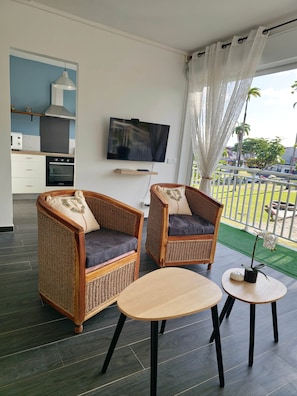 A living area with two wicker armchairs, a small table, a television, and a kitchen area with a stove and oven. - Amandine - vue mer Pointe-à-Pitre (Pointe-a-Pitre)
