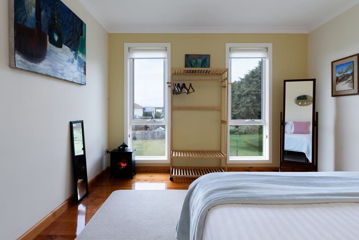 A bedroom with a bed, a wooden drying rack, a mirror, and a painting on the wall.