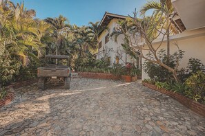 A stone-paved courtyard with a vehicle, surrounded by lush tropical plants and a building with a tiled roof. - Villa Catalina: San Pancho 5BR Estate w/ Pool, Ocean Views, Sleeps 10 (San Francisco)