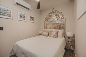 A bedroom with a large bed, decorative headboard, wall-mounted air conditioning, and framed pictures. - Dream Sayulita at Caivama: Corner Penthouse 2BR, Plunge Pool & Ocean Views (Sayulita)