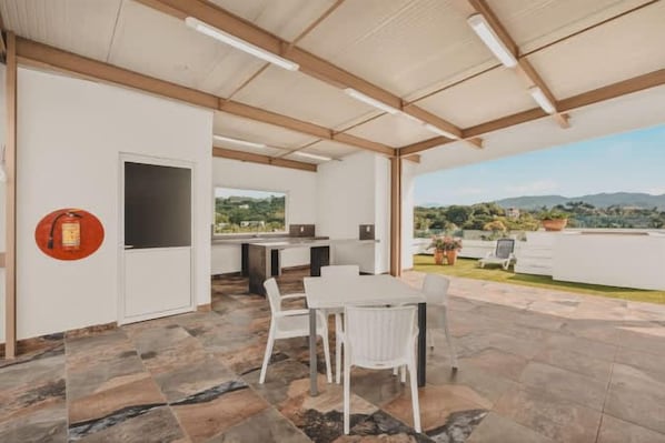 An open-plan living area with a dining table and chairs, a kitchen area, and a view of the countryside. - Mar Azul at La Esquina: San Pancho 2BR Sleeps 6, 1 Block to Beach (San Pancho)