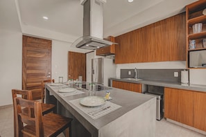 A modern kitchen with wooden cabinets, a stainless steel refrigerator, and a central island with seating. - Balconies Tranquillo at La Esquina: San Pancho 2BR, Ocean Views, Near Beach (San Pancho)