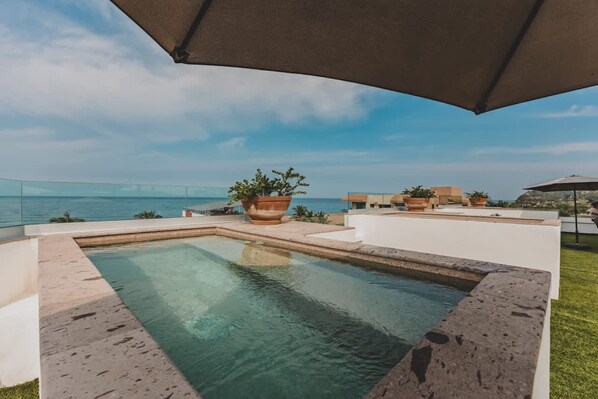 A swimming pool with a view of the sea, surrounded by potted plants and a large umbrella. - Balconies Tranquillo at La Esquina: San Pancho 2BR, Ocean Views, Near Beach (San Pancho)