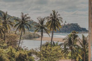 A beach view with palm trees and a rocky hill in the background. - Balconies Tranquillo at La Esquina: San Pancho 2BR, Ocean Views, Near Beach (San Pancho)