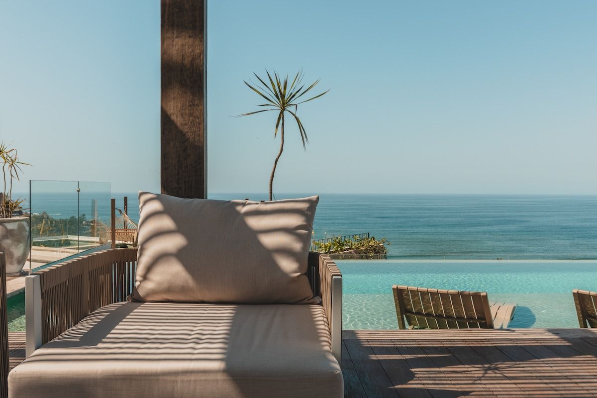 A lounge area with a view of the ocean, a palm tree, and a wooden deck.