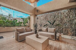 A modern living room with a stone wall, a sofa set, a coffee table, and a view of the outdoors. - Ceiba Tropical at Caivama: Sayulita 2BR, Jungle View & Plunge Pool (Sayulita)
