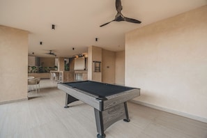 Taula de bitlles en una sala amb ventilador de sostre, zona de bar i menjador.
