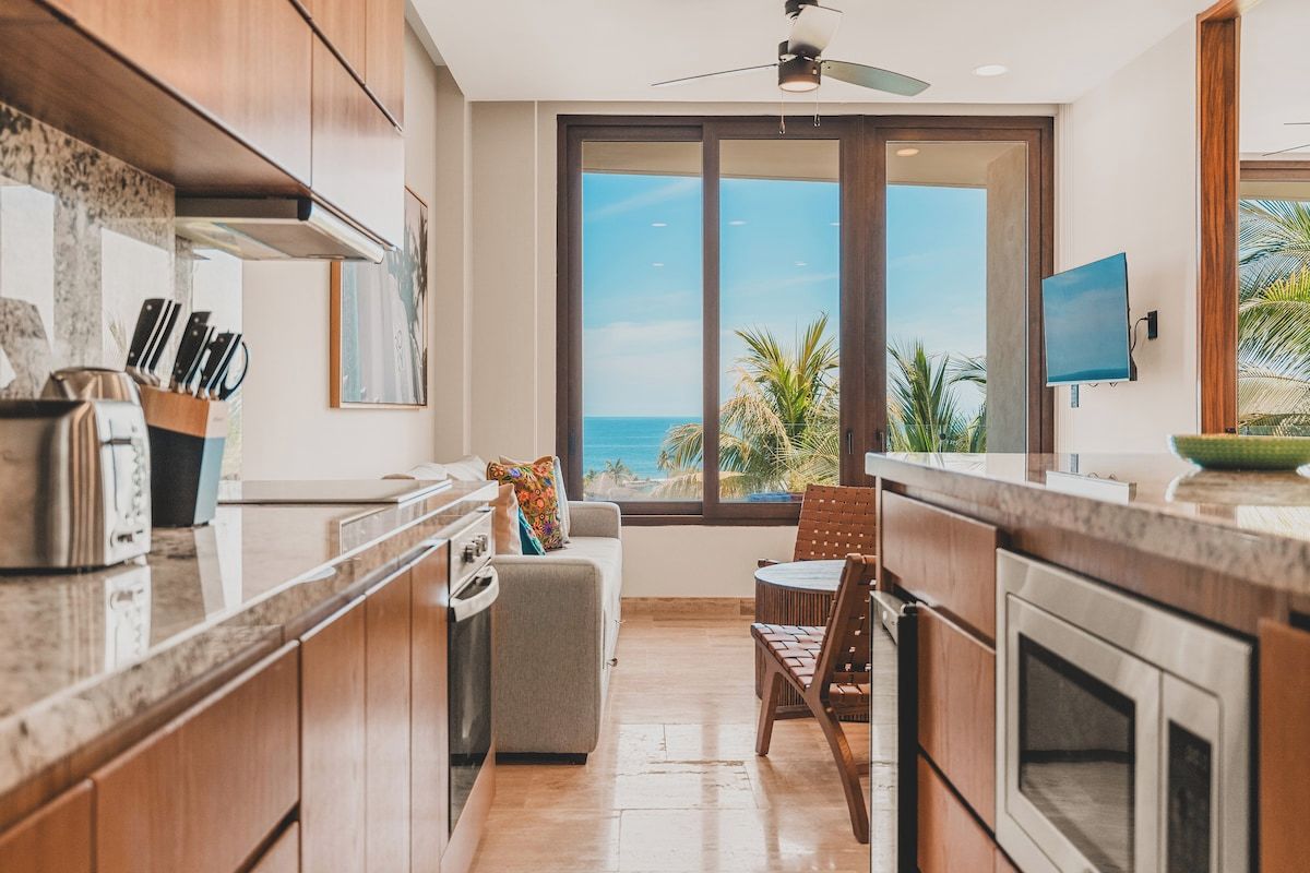 A modern kitchen with a view of the ocean, a dining area with a view, and a ceiling fan.